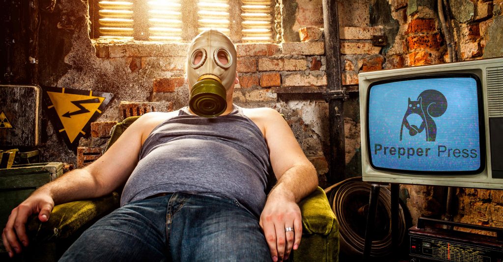 a man sits with his comy chair and crt television with gas mask on