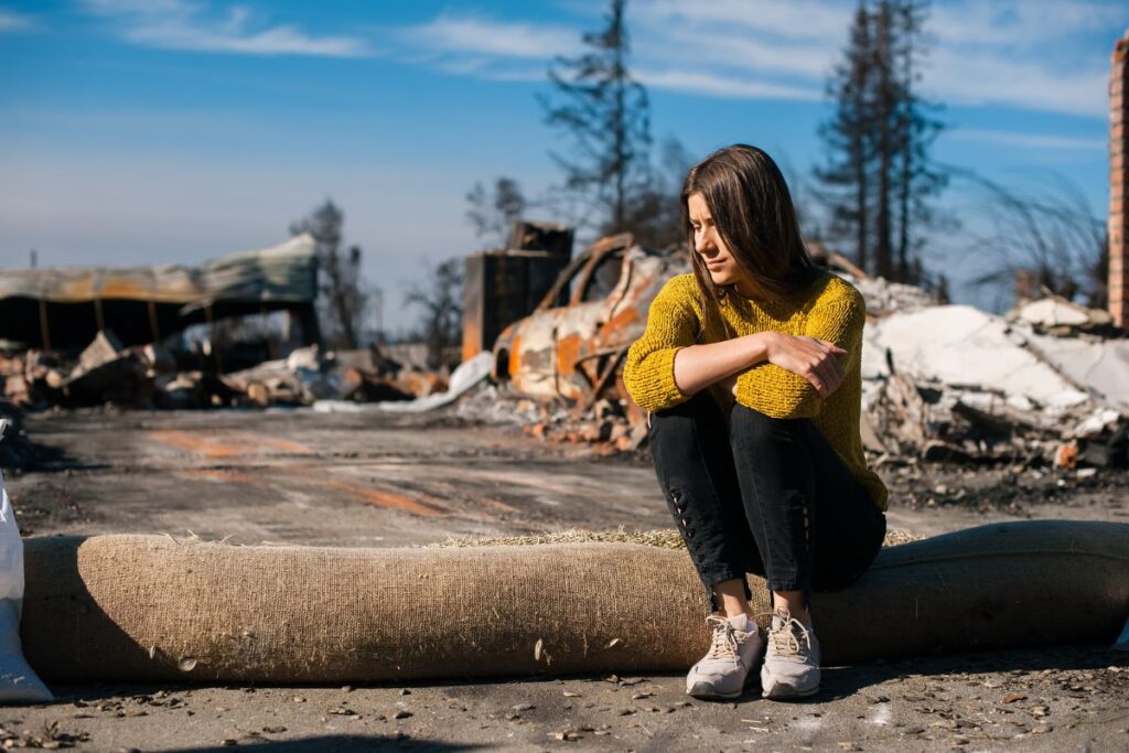 Woman sits in front of a burnt down house