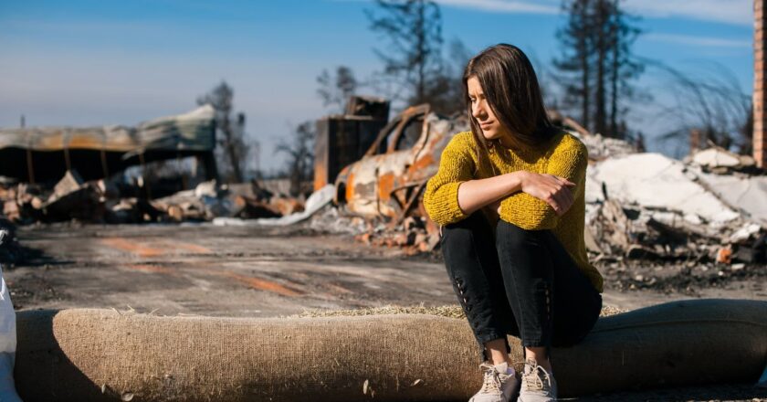 Woman sits in front of a burnt down house